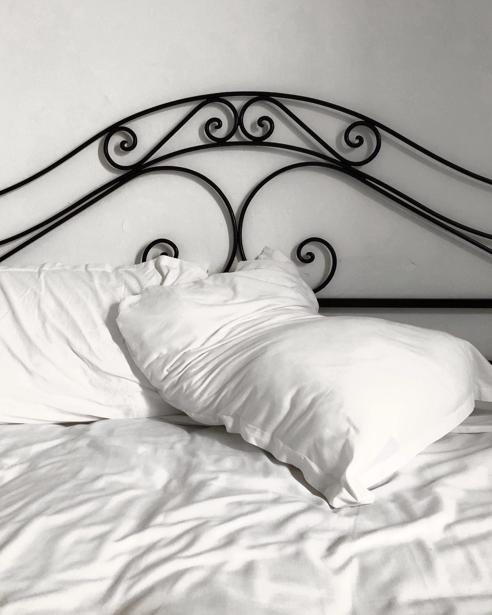 Crisp pearl white sheets and pillows below an iron headboard