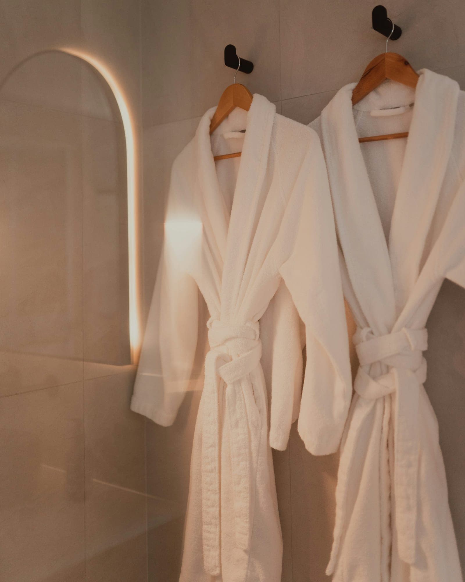 Two white bathrobes on wooden hangers